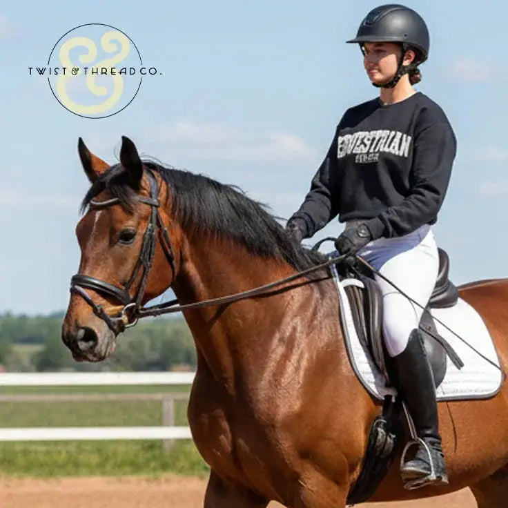 Equestrian athlete in black Twist & Thread Co. sweatshirt riding a bay horse in outdoor arena