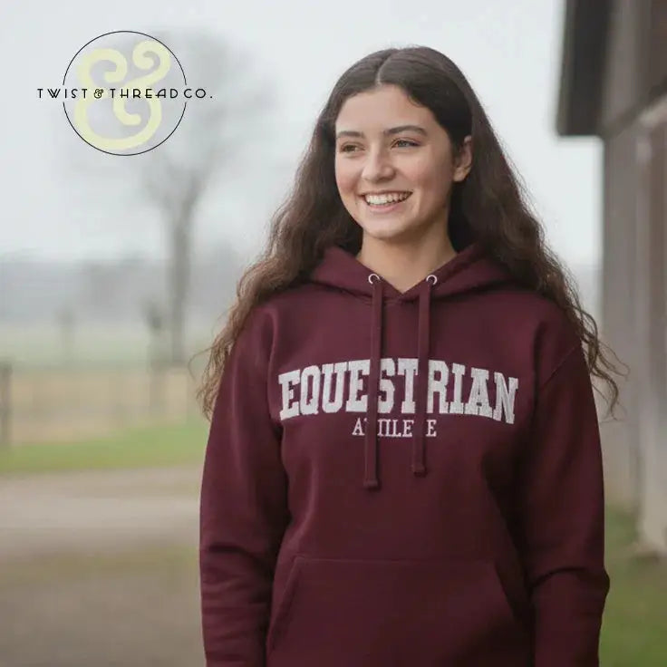 Smiling woman wearing maroon embroidered equestrian hoodie outdoors near barn