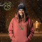 Smiling woman wearing a pink Festive AF hoodie and black beanie in a snowy outdoor setting