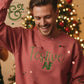 Smiling man wearing a red sweater with green text 'Festive AF' in front of a decorated Christmas tree