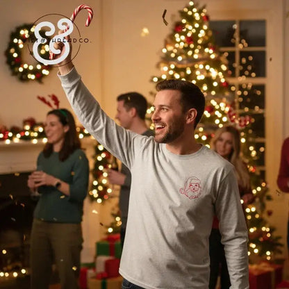 Smiling man in Santa sweatshirt holding candy cane at festive Christmas party with decorated tree and friends