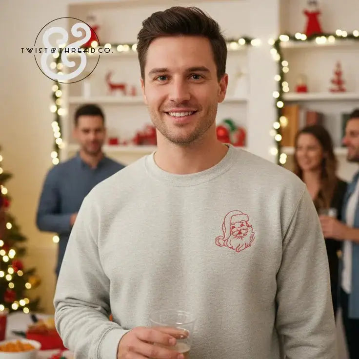 Smiling man wearing light gray sweatshirt with minimalist red Santa face design at festive holiday party