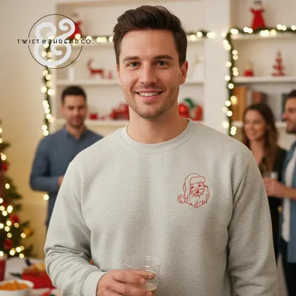 Smiling man wearing light gray sweatshirt with minimalist red Santa face design at festive holiday party