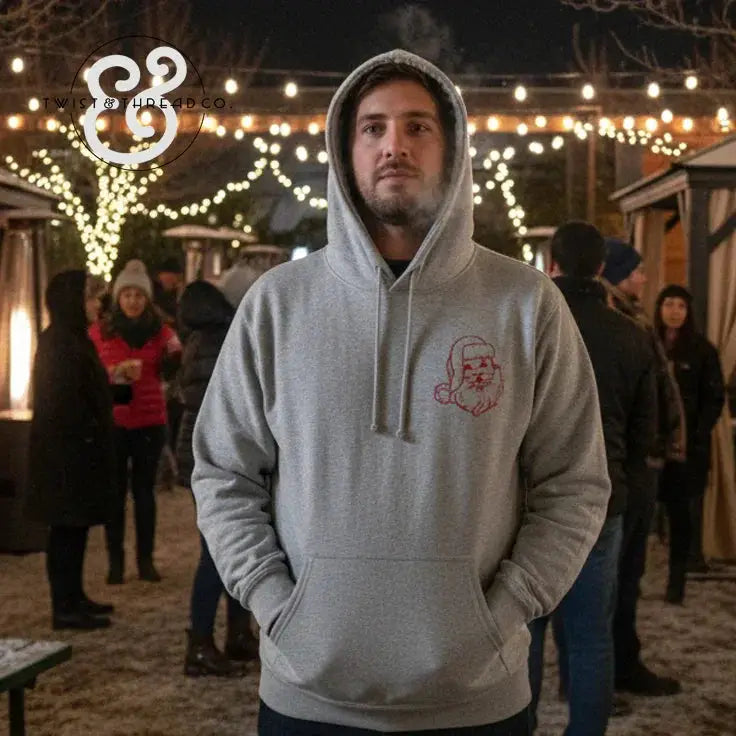 Man wearing grey hoodie with red Santa face print at outdoor holiday market with string lights