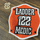 Embroidered orange patch with white and black text 'Ladder 122 Medic' on wooden surface