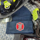 Navy blue firefighter knit beanie with Ladder 122 Medic patch on metal diamond plate floor with radio and helmet