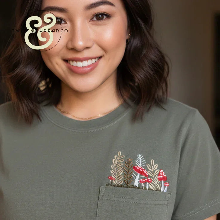 Woman in olive shirt with custom embroidered pocket featuring red mushrooms and plants