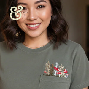 Woman in olive shirt with custom embroidered pocket featuring red mushrooms and plants
