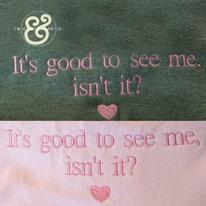 Green and pink fabric embroidery with the phrase "It's good to see me, isn't it?" and a small heart
