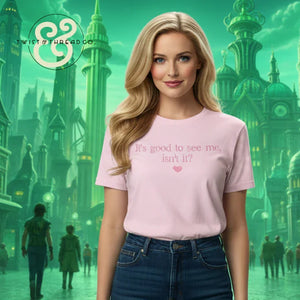 Blonde woman wearing pink t-shirt with 'It's good to see me, isn't it?' text, futuristic green city background