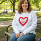 Woman wearing white sweatshirt with red heart applique by Twist & Thread Co. in park setting