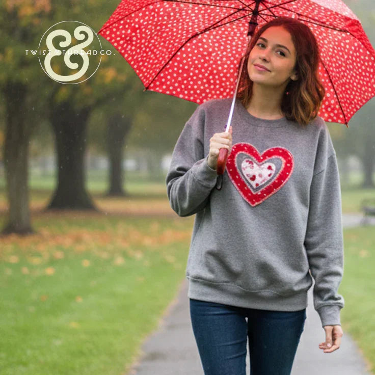 Woman holding red polka dot umbrella wearing grey heart applique embroidered sweatshirt outdoors