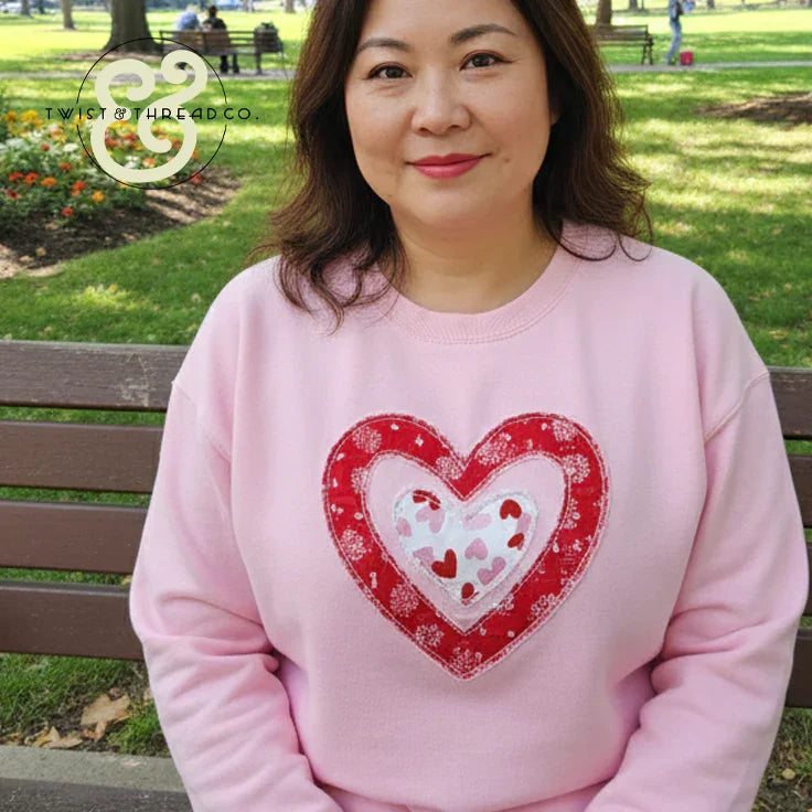 Woman wearing a pink heart applique embroidered sweatshirt by Twist & Thread Co. in park