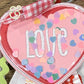 Embroidered pink heart with 'LOVE' text, colorful confetti, and red gingham ribbon from Twist & Thread Co.
