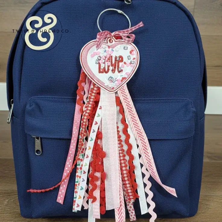 Embroidered heart-shaped 'Love' keychain with pink and red ribbons on navy backpack from Twist & Thread Co.