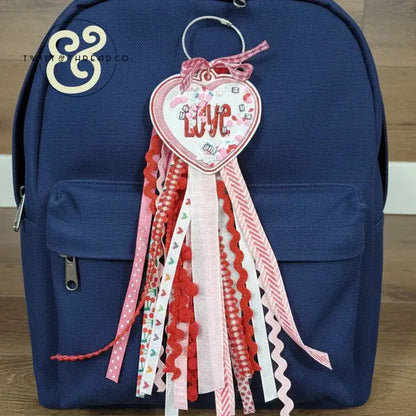 Embroidered heart-shaped 'Love' keychain with pink and red ribbons on navy backpack from Twist & Thread Co.