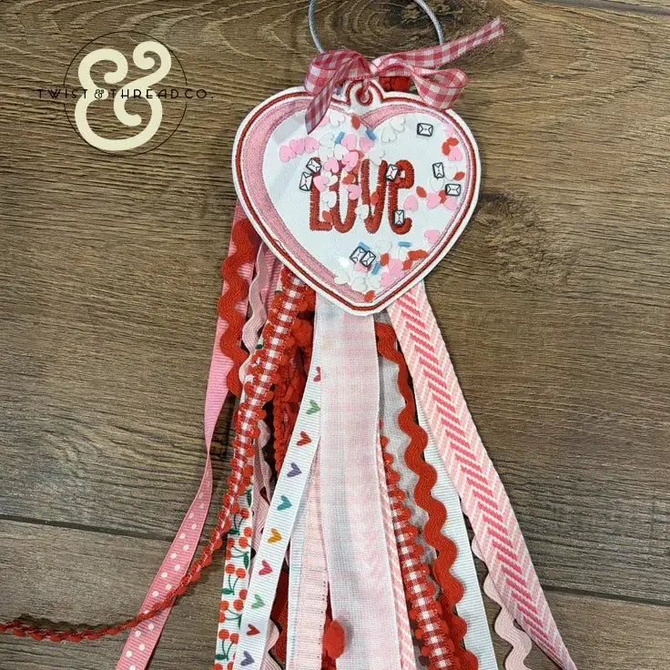 Heart-shaped embroidered LOVE wall hanging with pink and red ribbons, Twist & Thread Co.