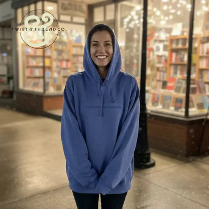 Smiling woman wearing blue hoodie with text outside bookstore at night, cozy casual fashion