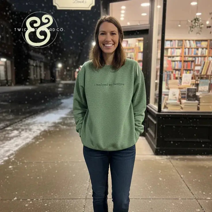 Smiling woman in green sweatshirt reading past bedtime standing outside snowy bookstore at night