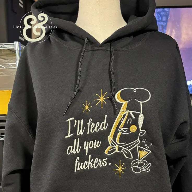 Black hoodie with embroidered chef cartoon and text I'll feed all you fuckers in white and gold