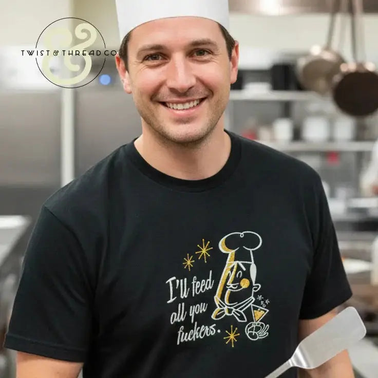 Smiling male chef wearing black embroidered T-shirt with humorous kitchen quote in commercial kitchen
