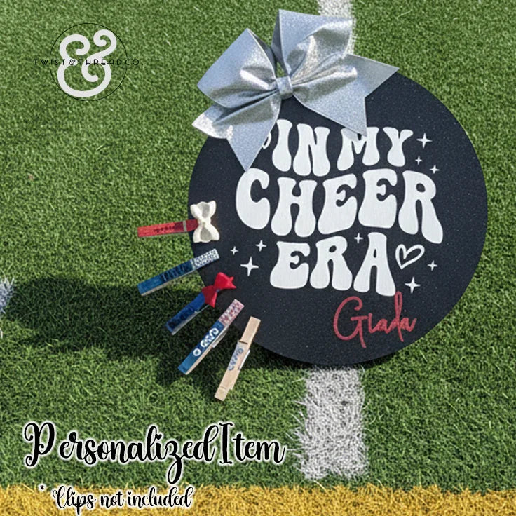 Personalized cheer era sign with silver bow on turf, custom name, and decorative clothespins