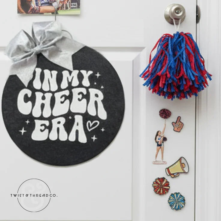 Cheerleading door sign with 'In My Cheer Era,' silver bow, blue and red pompom, cheer stickers