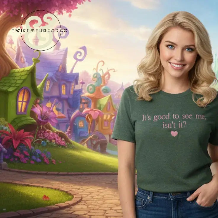 Smiling woman in green T-shirt with text 'It's good to see me, isn't it?' in a whimsical fantasy village backdrop