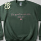 Green sweatshirt with pink text embroidered saying 'It's good to see me, isn't it?' and a heart below