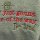 Close-up of gray fabric with embroidered red and brown text reading "I'm just gonna be out of the way I'm tired"