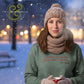 Woman in winter knit hat and scarf holding red mug in snowy outdoor setting with holiday sweater