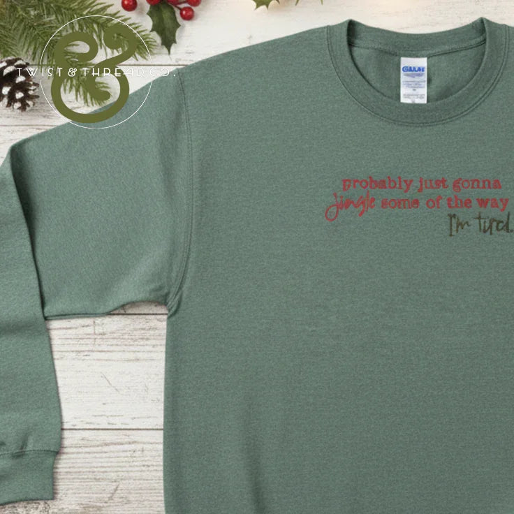 Green crewneck sweatshirt with festive red and brown text, holiday pine cones and berries background
