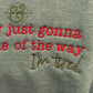 Close-up of gray fabric with embroidered red and brown text reading "I'm just gonna be out of the way I'm tired"