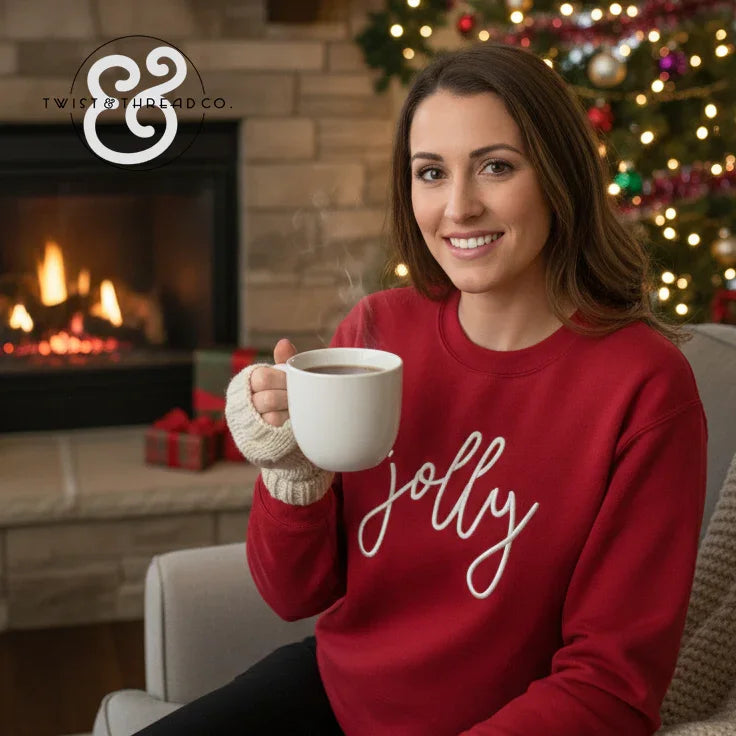 Smiling woman in red 'jolly' Christmas sweater holding a steaming mug by a decorated tree and fireplace