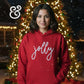 Young woman wearing red 'jolly' hoodie with Christmas lights and tree in background