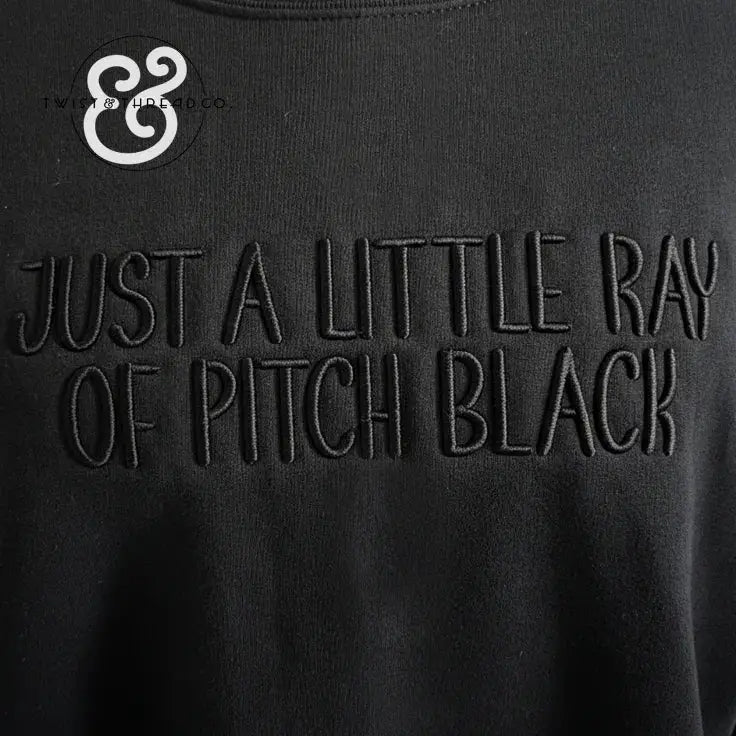 Black fabric with embroidered text reading Just a Little Ray of Pitch Black and Twist & Thread Co logo
