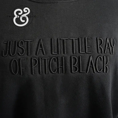 Black fabric with embroidered text reading Just a Little Ray of Pitch Black and Twist & Thread Co logo