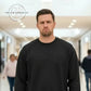 Man wearing a black sweatshirt with embossed text 'Just a little ray of pitch black' in a modern indoor corridor