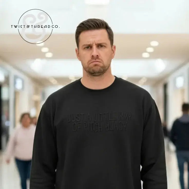 Man wearing a black sweatshirt with embossed text 'Just a little ray of pitch black' in a modern indoor corridor