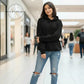 Young woman wearing a black hoodie and ripped blue jeans standing in a shopping mall hallway