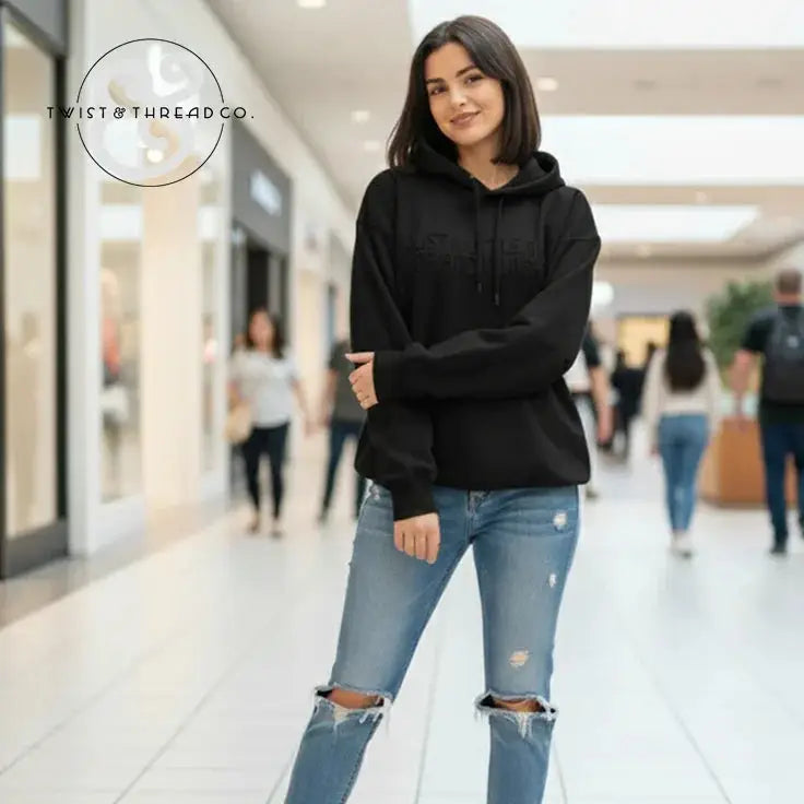 Young woman wearing a black hoodie and ripped blue jeans standing in a shopping mall hallway