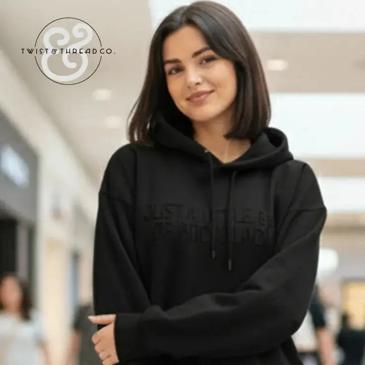 Smiling woman wearing black hoodie with subtle text in a bright indoor shopping mall