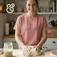 Woman smiling while kneading sourdough dough in kitchen, wearing pink shirt saying keep this buch alive