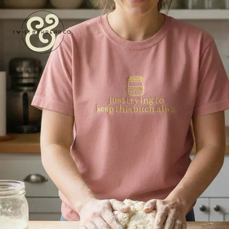 Person wearing dusty rose t-shirt with yellow text and jar graphic, kneading dough in kitchen