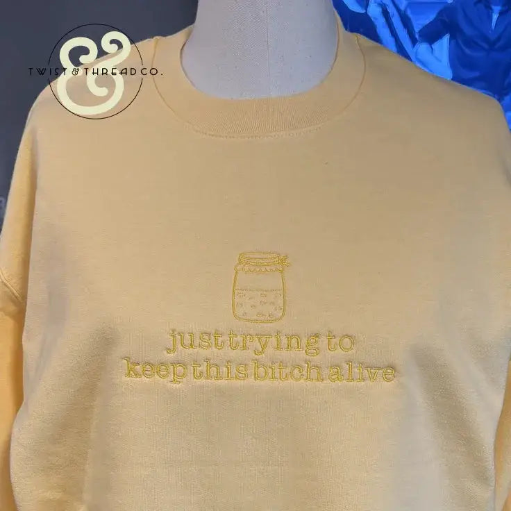 Yellow sweatshirt with embroidered jar and text just trying to keep this bitch alive by Twist & Thread Co.