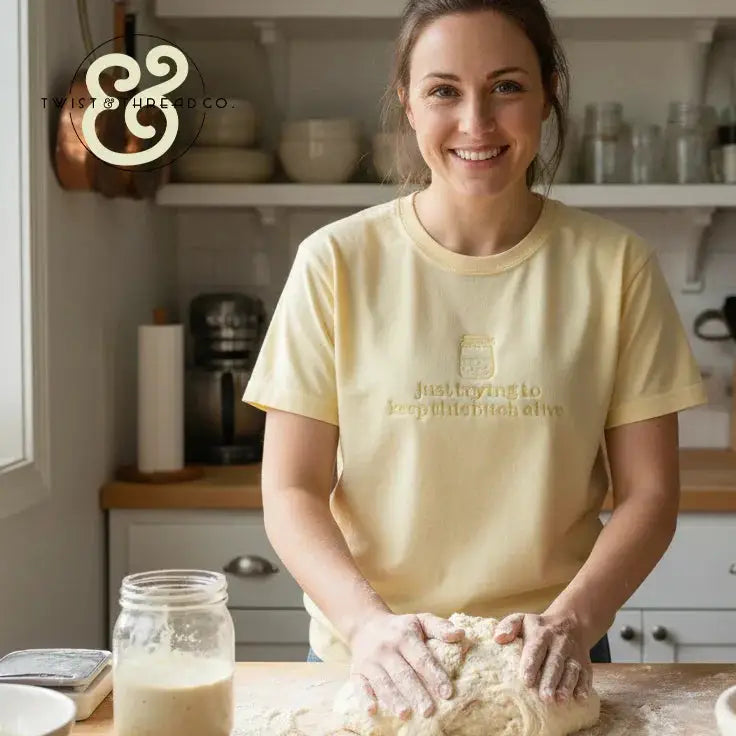 Smiling woman kneading dough in bright kitchen wearing light yellow shirt with humorous text