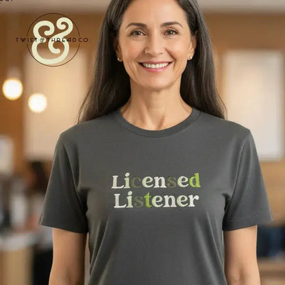 Smiling woman wearing a dark gray embroidered t-shirt with 'Licensed Listener' text, casual indoor setting