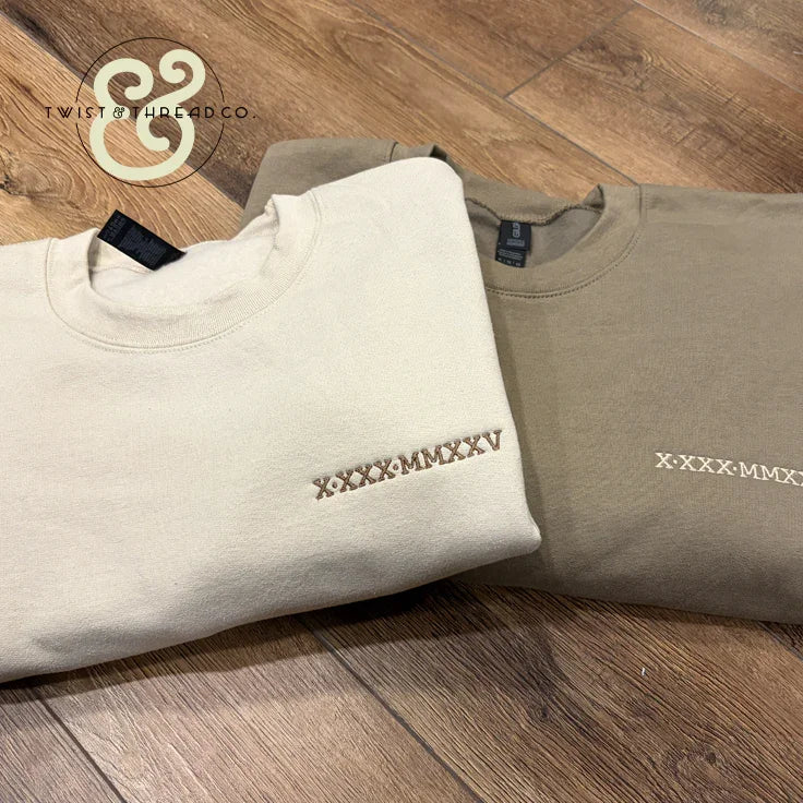 Twist & Thread Co. embroidered beige sweatshirts with Roman numerals on wood floor