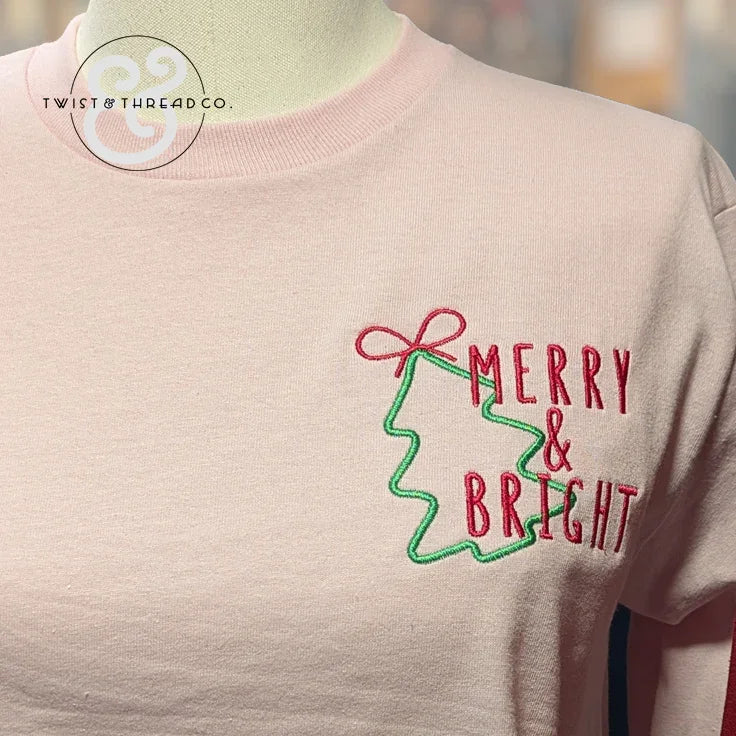 Pink sweatshirt with embroidered green Christmas tree and red 'Merry & Bright' text
