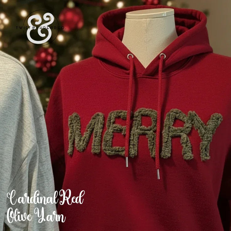 Cardinal red hoodie with fuzzy olive green 'MERRY' text, Christmas tree background